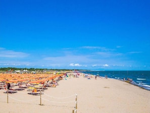 A beach with rows of sunbeds and umbrellas, a clear sky, and the ocean in the background. - Comfy Stay Near the Beach in Rosolina Mare (Rosolina)