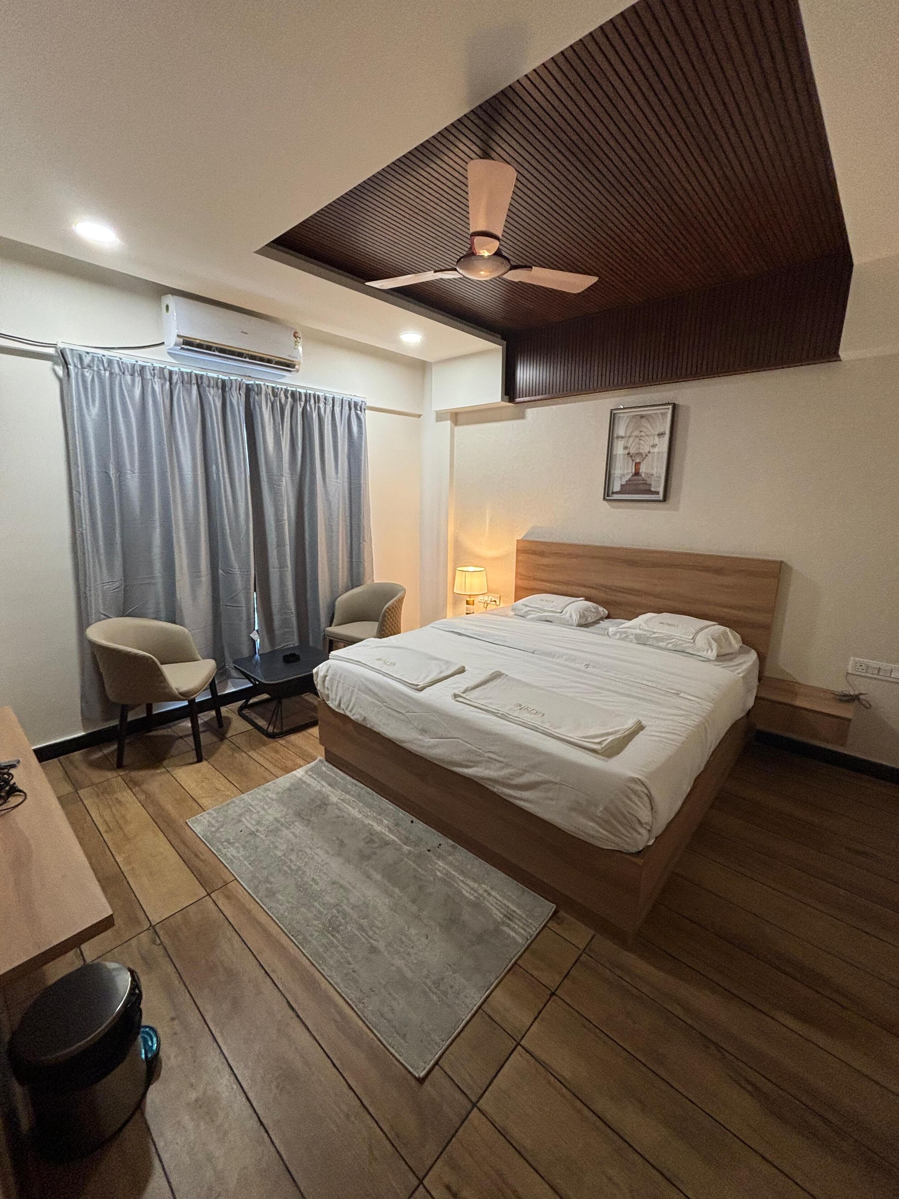 Un dormitorio con una cama, un escritorio, dos sillas, un ventilador de techo y un equipo de aire acondicionado.