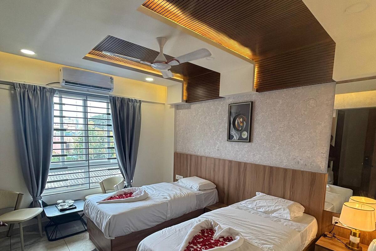 A hotel room with two beds, a desk, a chair, a desk lamp, and a ceiling fan.