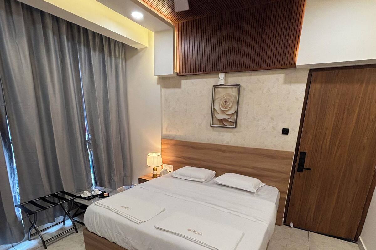 A modern hotel room with a large bed, a ceiling fan, a wooden headboard, a nightstand with a lamp, and a door.