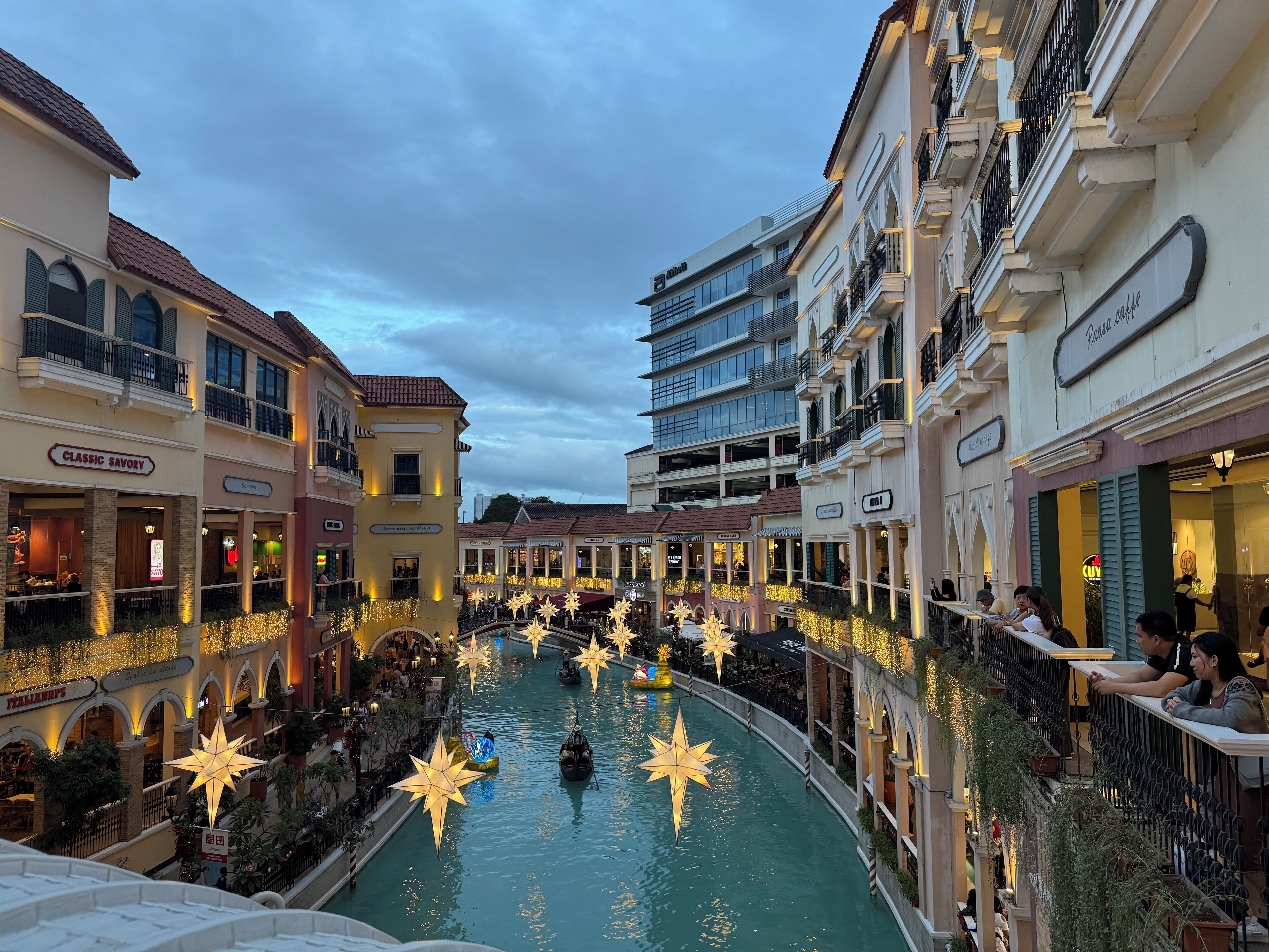A canal with star-shaped decorations, surrounded by multi-story buildings with various shops and restaurants.