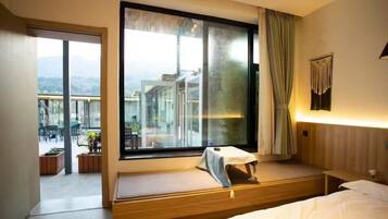 A hotel room with a large window, a bed, a bedside table, and a view of the cityscape.