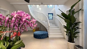 Een ruim interieur met een gebogen trap, een blauwe met kussens beklede bank en potplanten.