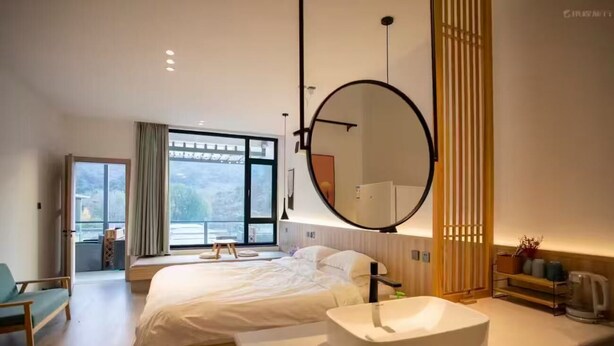 Een moderne hotelkamer met een groot bed, een ronde spiegel, een witte wastafel en uitzicht op het groen.