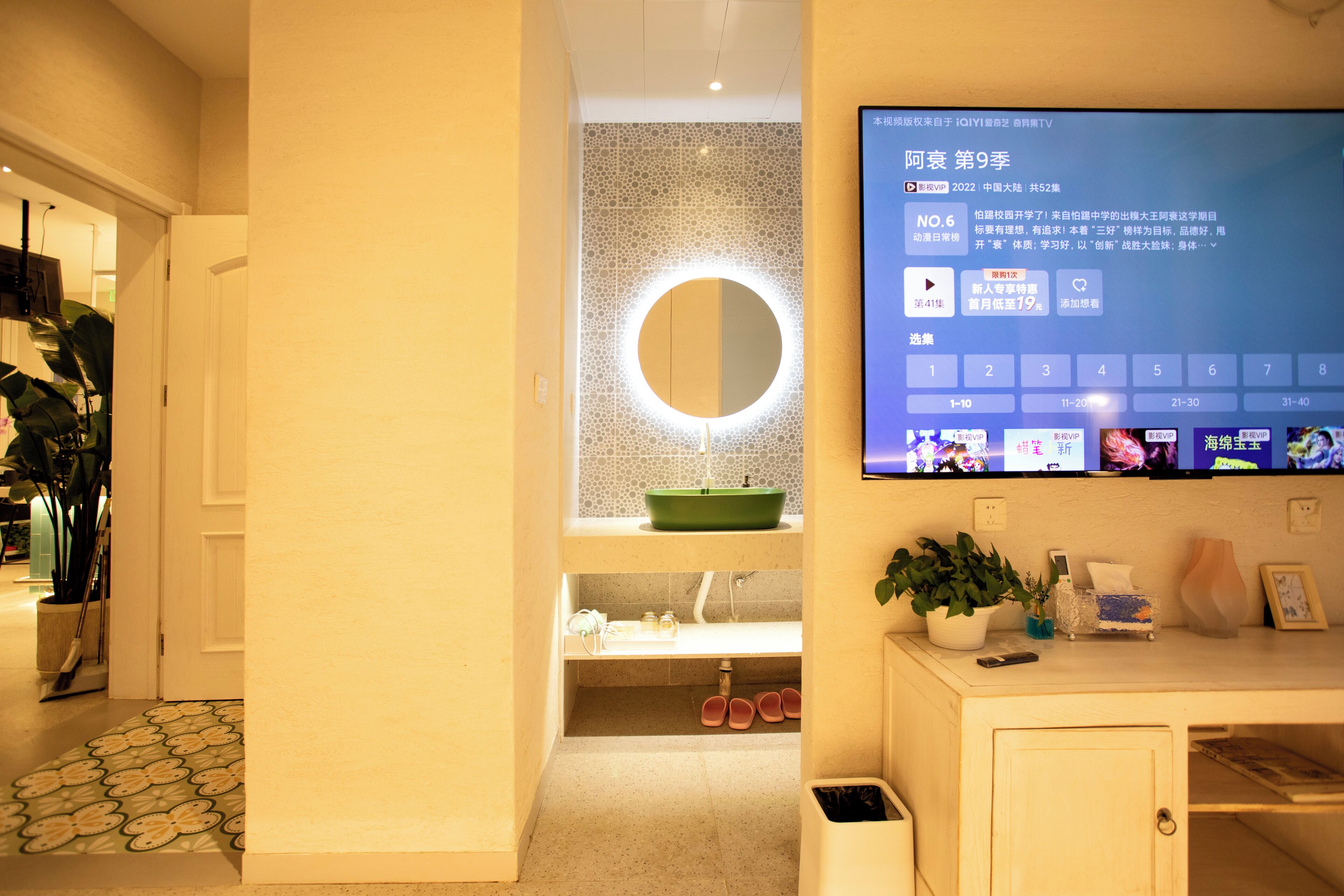 A bathroom with a mirror, sink, and a television mounted on the wall displaying a program.