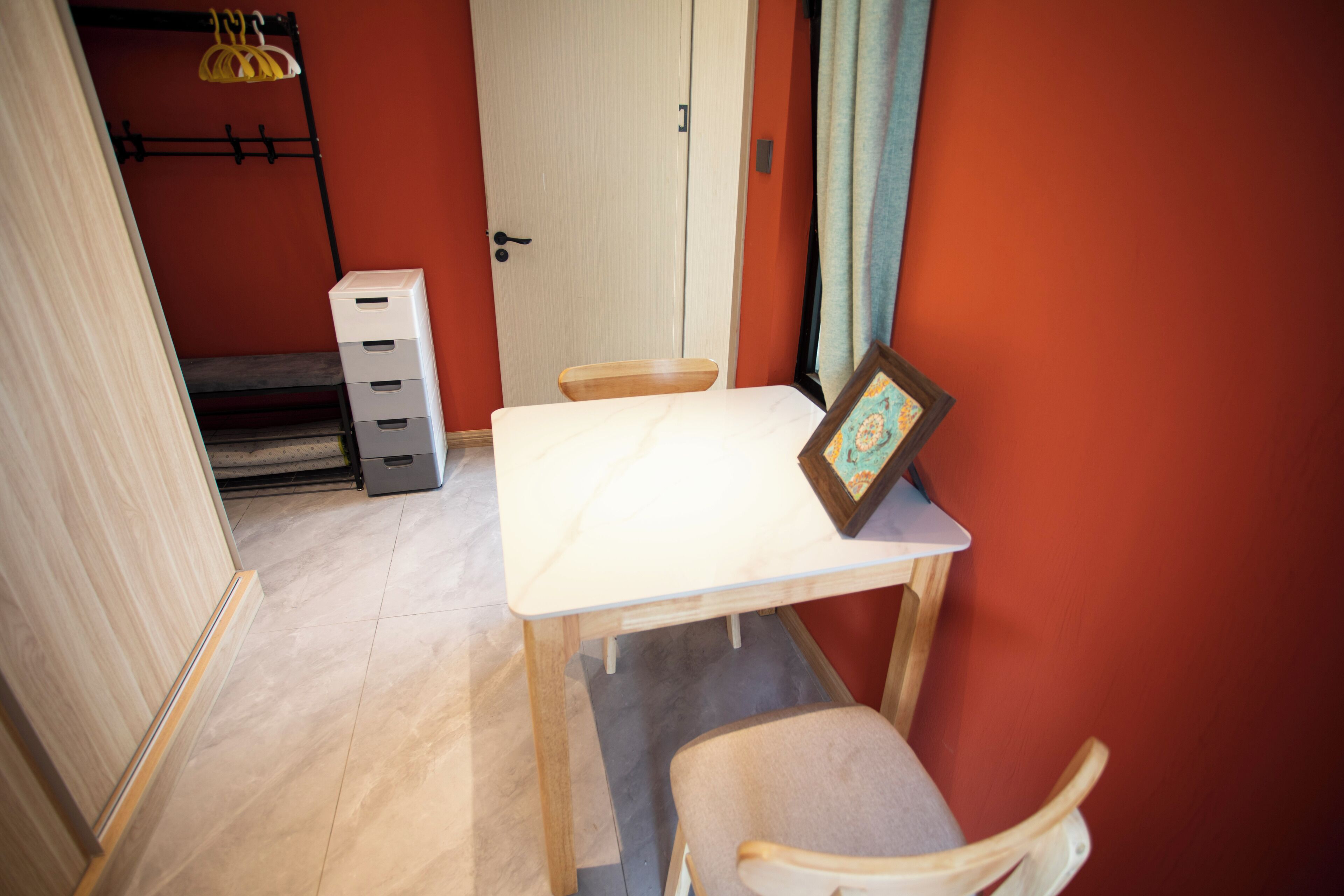 Una habitación pequeña con una mesa blanca y una silla, una puerta y un perchero con un objeto amarillo colgado.
