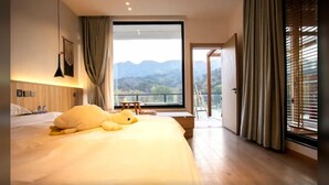 Een hotelkamer met een groot bed, uitzicht op bergen en een balkon met een tafel en stoelen.