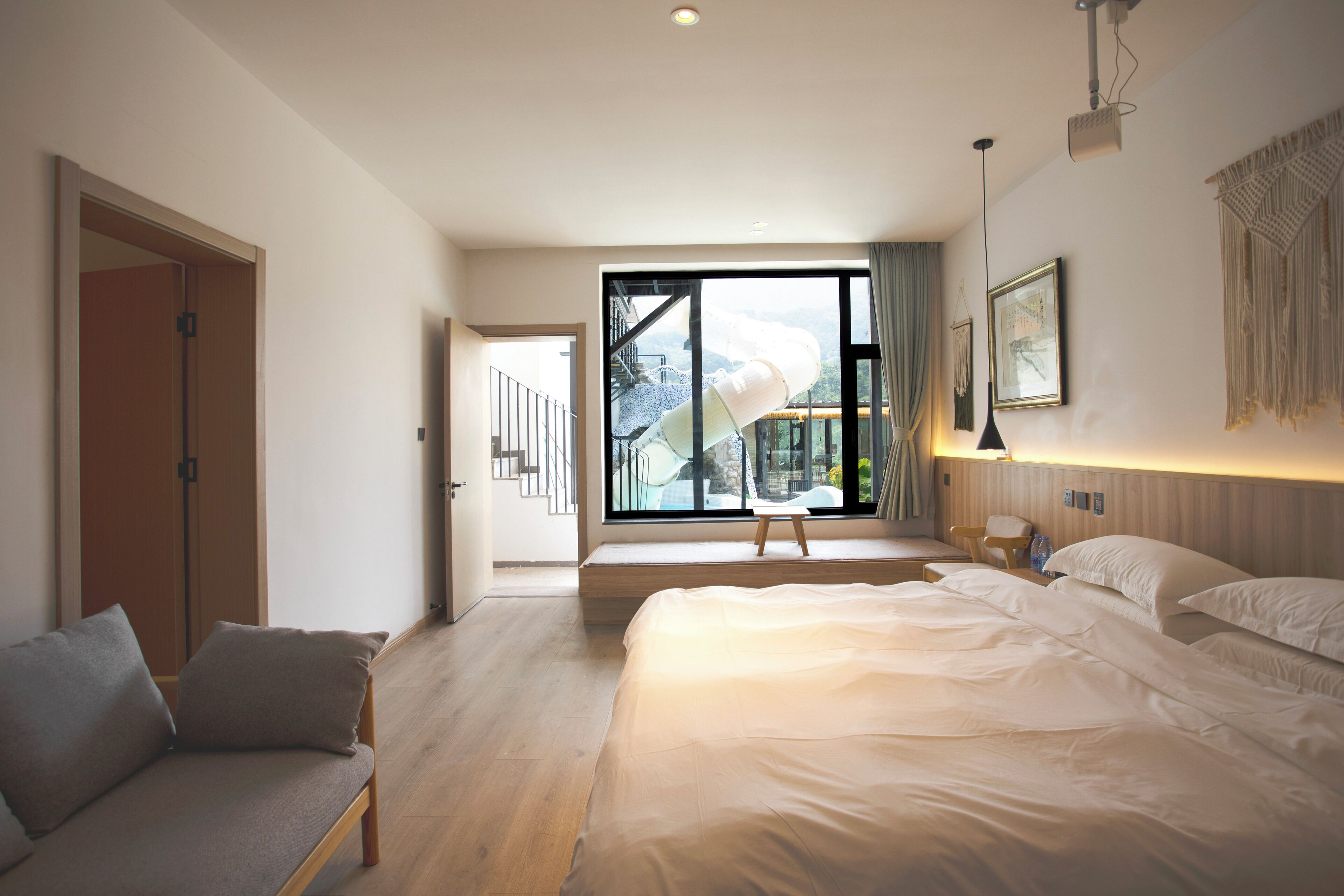 A modern hotel room with a large bed, a sofa, a small table, and a view of a mountain through a large window.