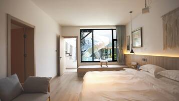 A modern hotel room with a large bed, a sofa, a small table, and a view of a mountain through a large window.