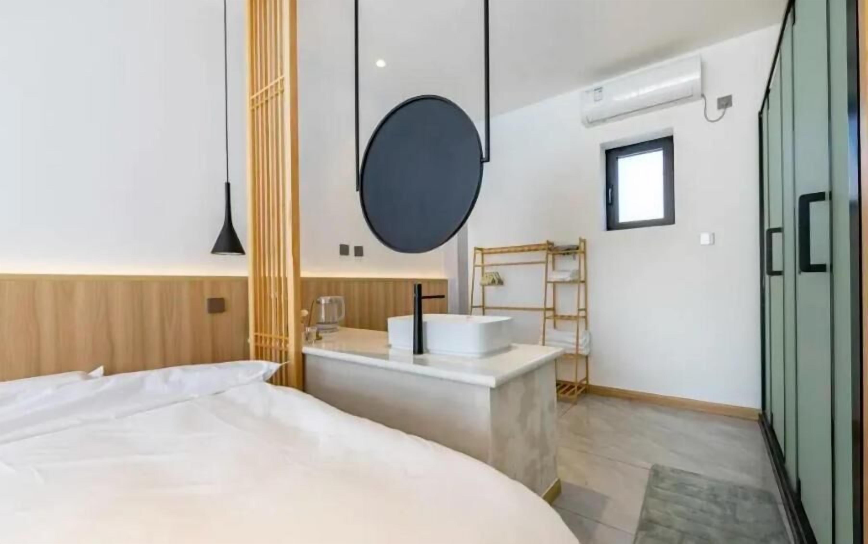 A modern bedroom with a large bed, a round mirror, a small bathroom with a sink and a ladder, and a wardrobe.