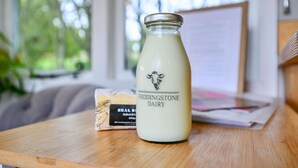 A glass bottle of Chiddingtone Dairy milk on a wooden table with a whiteboard and a bag of bread in the background. - Badger Shepherds Hut - a holiday let that sleeps 2 guests in 1 bedroom (Hartfield)