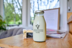 A glass bottle of Chiddingtone Dairy milk on a wooden table with a whiteboard and a bag of bread in the background. - Badger Shepherds Hut - a holiday let that sleeps 2 guests in 1 bedroom (Hartfield)