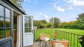 A wooden deck with wicker chairs and a small table, overlooking a green lawn and trees. - Badger Shepherds Hut -  a holiday let that sleeps 2 guests  in 1 bedroom (Hartfield)