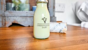 A glass bottle of Chiddington Dairy on a wooden table.