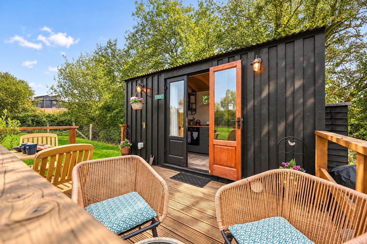 A wooden cabin with a sliding door, wicker furniture, and a garden view.