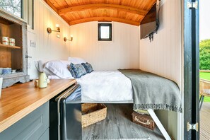 A cozy bedroom with a wooden ceiling, a small window, a bed with white bedding, and a wooden nightstand with a lamp. - Deer Shepherds Hut - a holiday let that sleeps 2 guests in 1 bedroom (Hartfield)