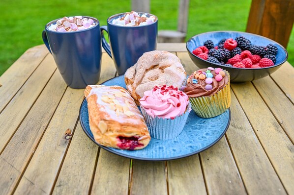 A wooden table with a plate of pastries, two mugs, and a bowl of berries.
