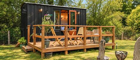 A small wooden cabin with a deck, outdoor seating, and a garden.