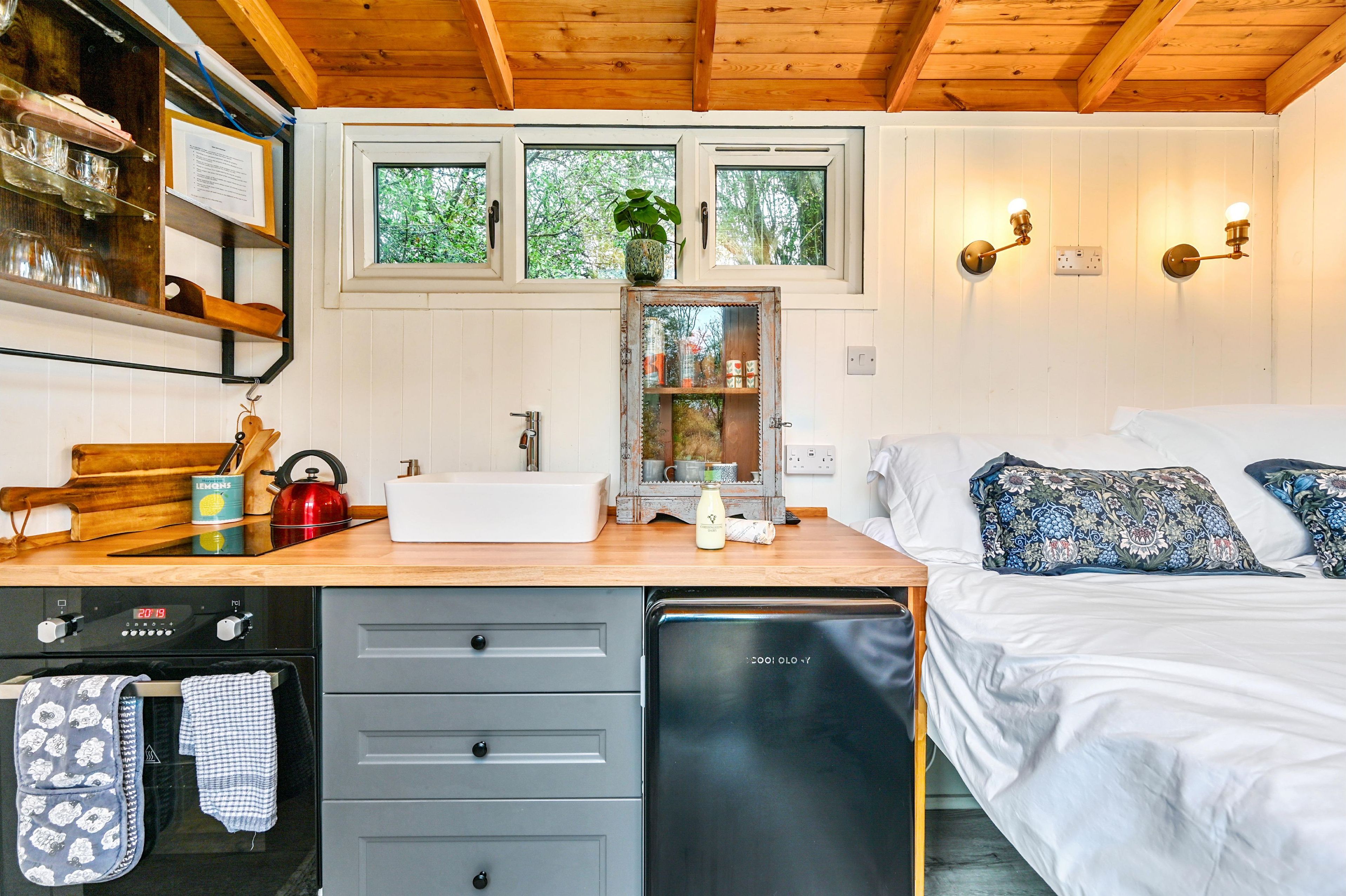 A compact bedroom with a bed, bedside table, and a window with a view of trees.