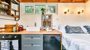 A compact bedroom with a bed, bedside table, and a window with a view of trees.