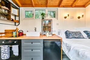 A compact bedroom with a bed, bedside table, and a window with a view of trees. - Deer Shepherds Hut -  a holiday let that sleeps 2 guests  in 1 bedroom (Hartfield)