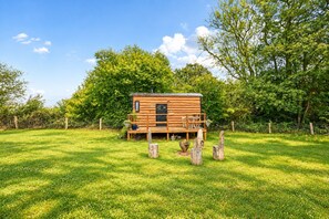 A wooden cabin with a deck, surrounded by a fenced yard and trees. - Stag Shepherds Hut -  a holiday let that sleeps 4 guests  in 1 bedroom (Hartfield)