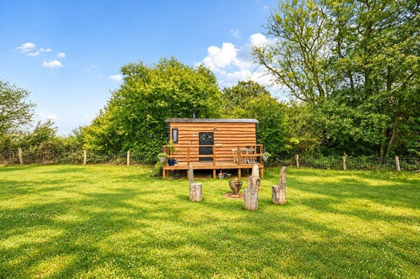 A wooden cabin with a deck, surrounded by a fenced yard and trees. - Stag Shepherds Hut - a holiday let that sleeps 4 guests in 1 bedroom (Hartfield)