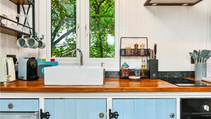A kitchen with a white sink, wooden countertop, and blue cabinets. There is a window with a view of trees. - Stag Shepherds Hut -  a holiday let that sleeps 4 guests  in 1 bedroom (Hartfield)