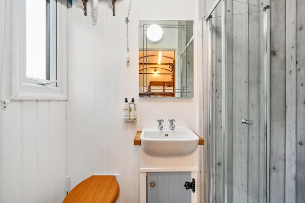 A bathroom with a white sink, wooden cabinet, and a mirror. - Stag Shepherds Hut -  a holiday let that sleeps 4 guests  in 1 bedroom (Hartfield)