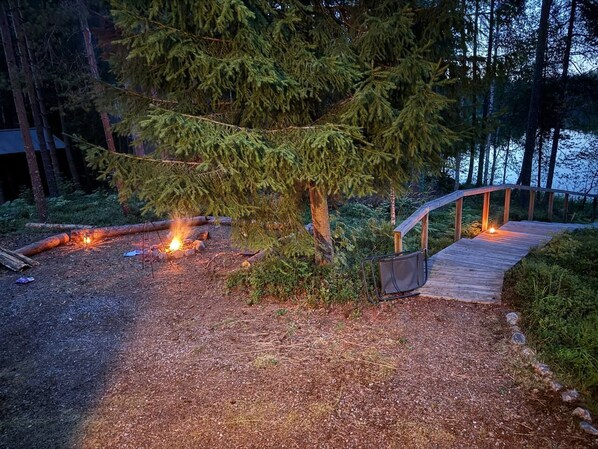 A wooden deck with a metal railing, surrounded by trees and a gravel path. - Chalet Zen By Saimaa Hills (Miettilä)