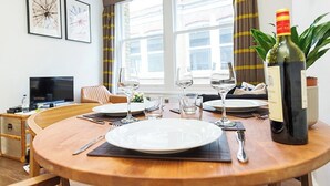 A dining table set with plates, glasses, and cutlery, a bottle of wine, and a television in the background.