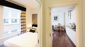 A modern hotel room with a large bed, a dining area with a table and chairs, and a kitchen area with a sink and countertop.