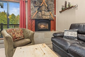 Un salón acogedor con chimenea de piedra, sofás de cuero y vistas a árboles a través de amplios ventanales.