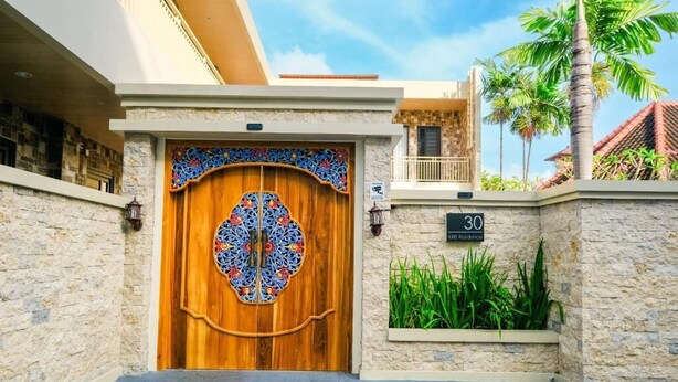 A wooden door with a decorative glass panel, a stone wall, and a sign indicating the number 30. - Kris Residence Sanur (Denpasar)