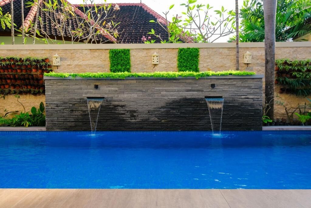 A swimming pool with a stone wall and two water features.