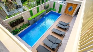 A rooftop pool with a waterfall feature, surrounded by lounge chairs and greenery. - Kris Residence Sanur (Denpasar)