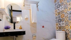 A bathroom with a white toilet, a black sink with a mirror, and a patterned tile wall. - Kris Residence Sanur (Denpasar)