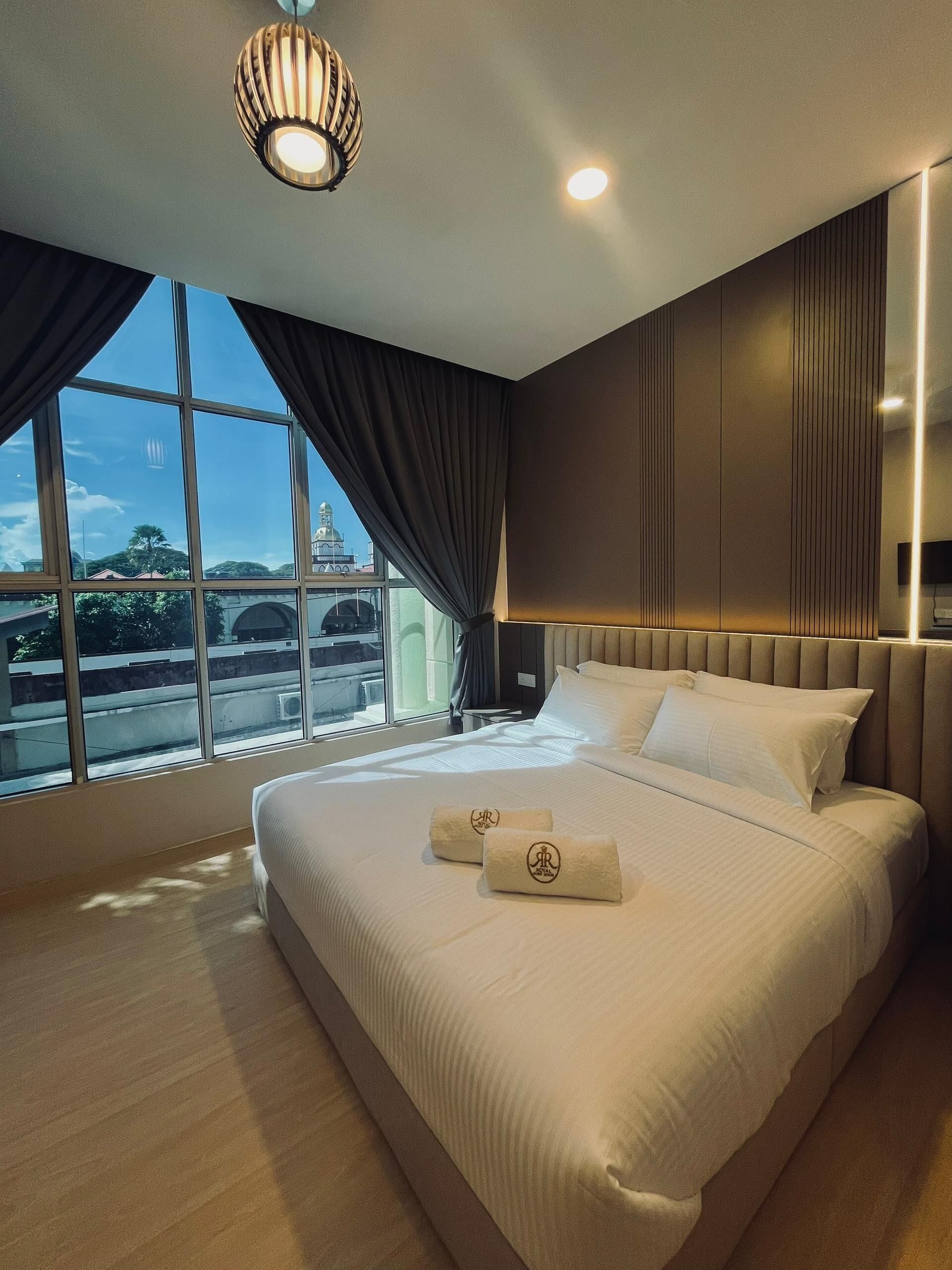 Une chambre d’hôtel moderne dotée d’un grand lit, offrant une vue sur le paysage urbain, et agrémentée d’un luminaire au plafond au design original.