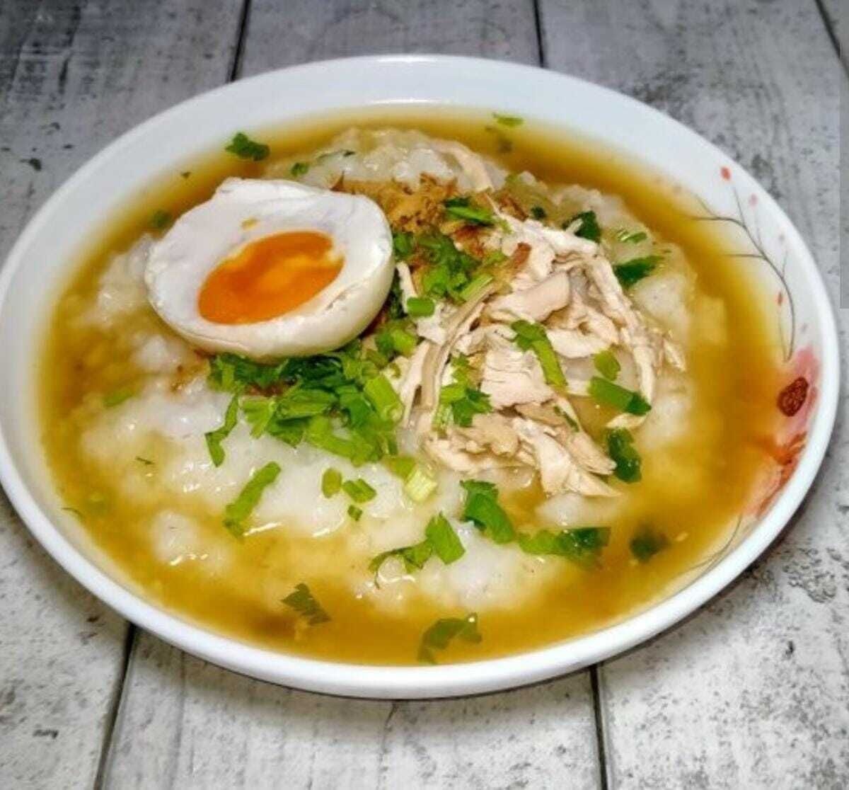 A bowl of soup with shredded chicken, a half-boiled egg, and chopped green onions.
