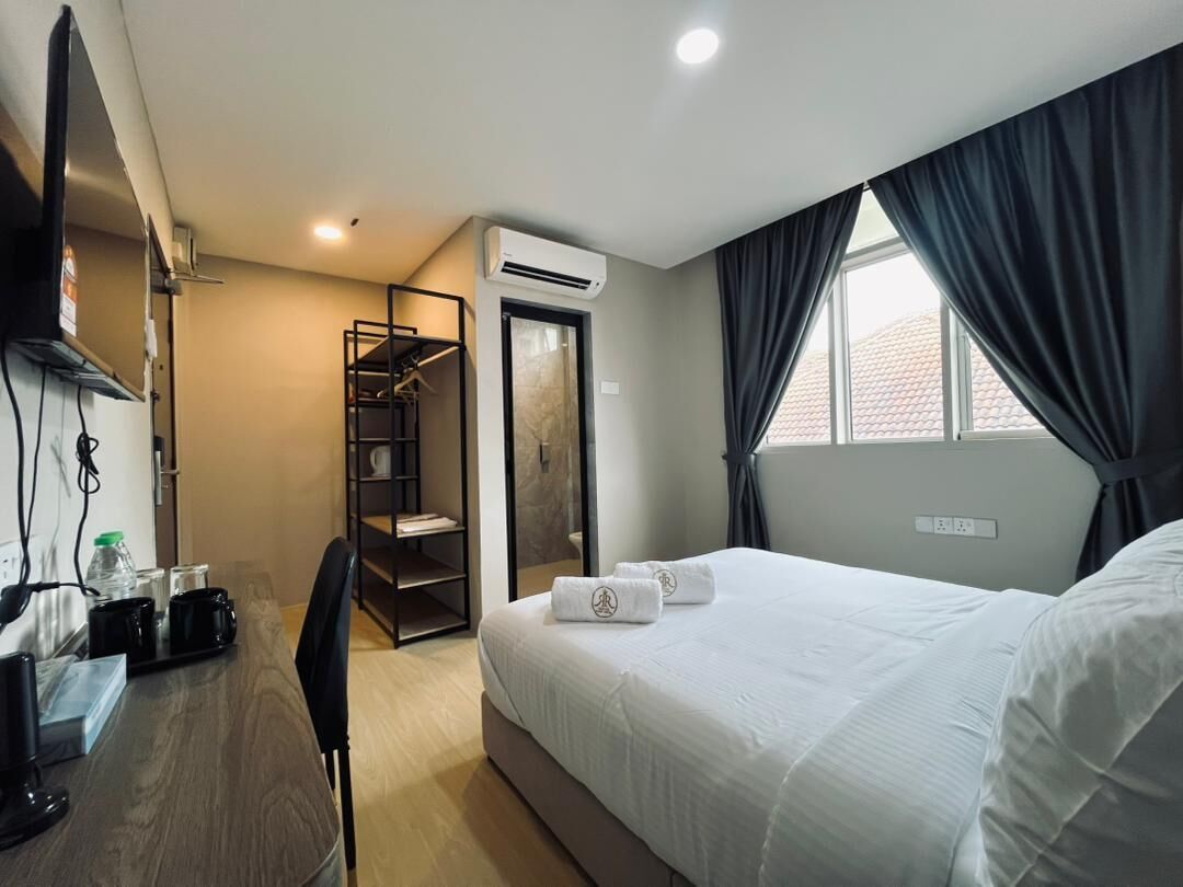 A hotel room with a bed, a desk with a chair, a wardrobe, and an air conditioning unit.