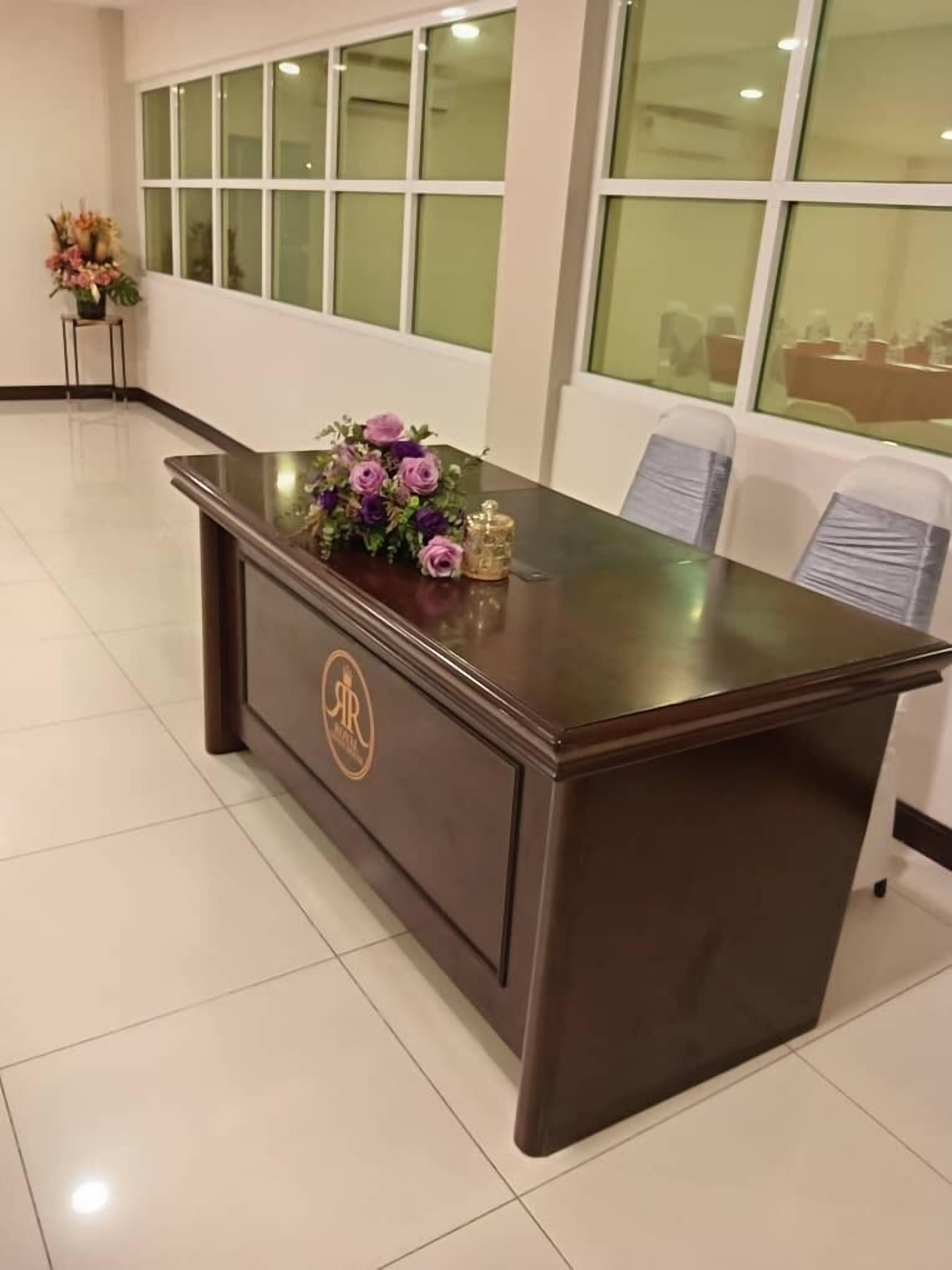 A reception desk with a logo, a vase of flowers, and a window in the background.