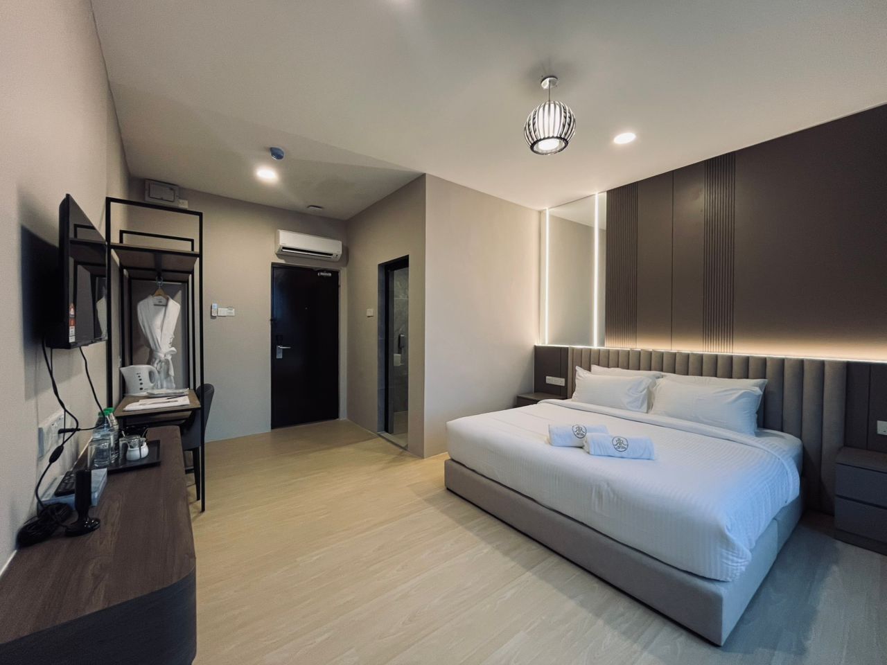 A modern hotel room with a large bed, a desk with a chair, a flat-screen TV mounted on the wall, and a ceiling light fixture.