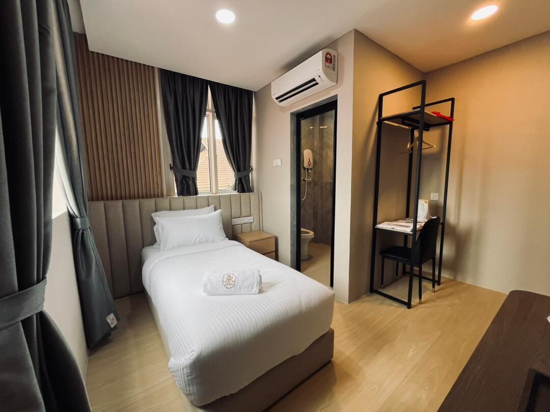 A hotel room with a bed, a desk, a chair, an air conditioning unit, and a shower area.