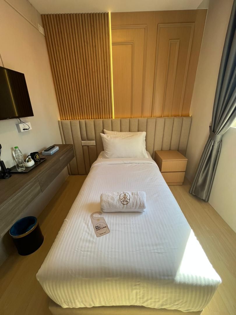 Ein Hotelzimmer mit Bett, Nachttisch, Fernseher, Fenster mit Vorhängen und einem an der Wand montierten Fernseher.
