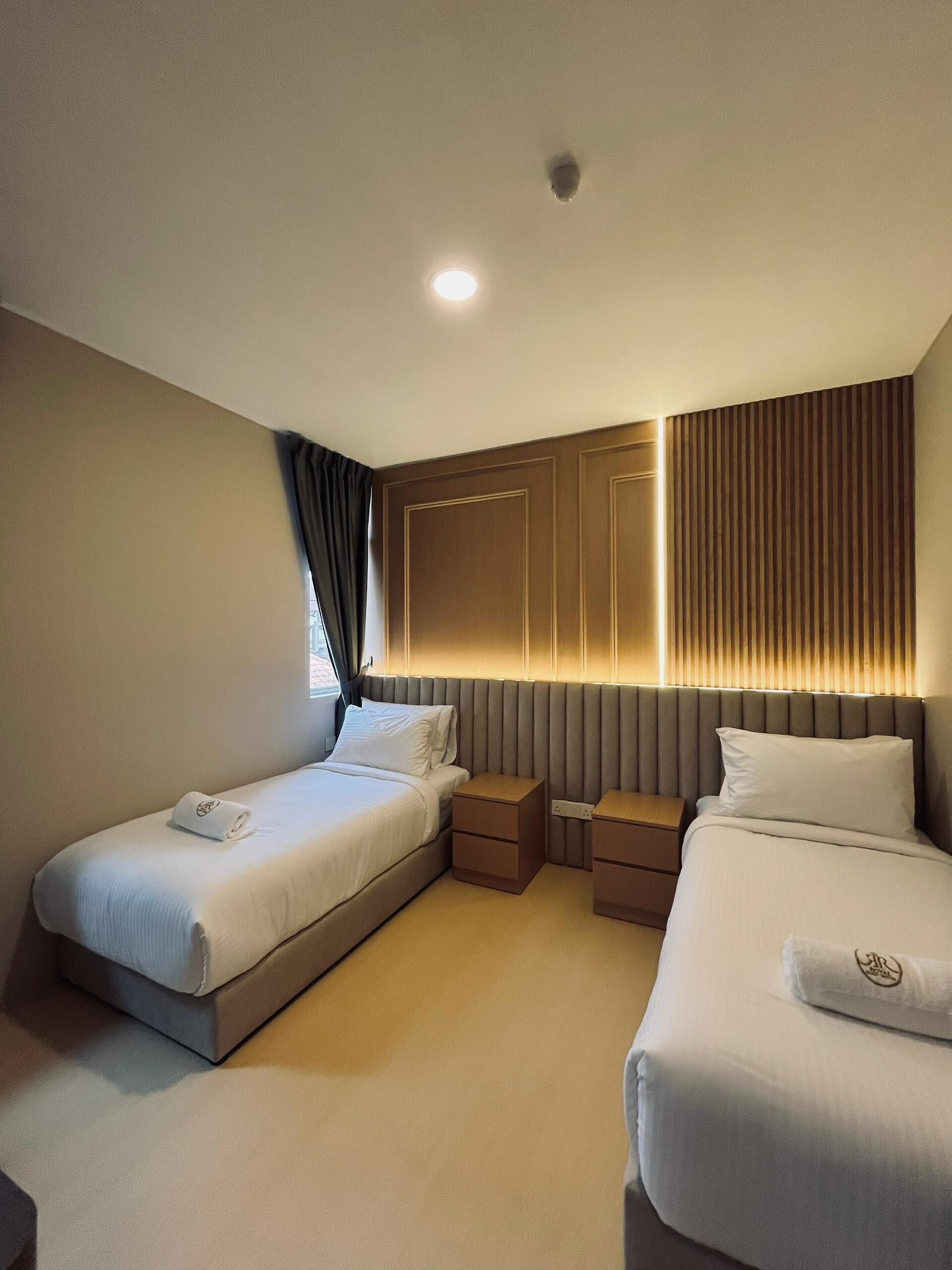 Une chambre d’hôtel avec deux lits, une table de chevet et une lampe fixée au mur.