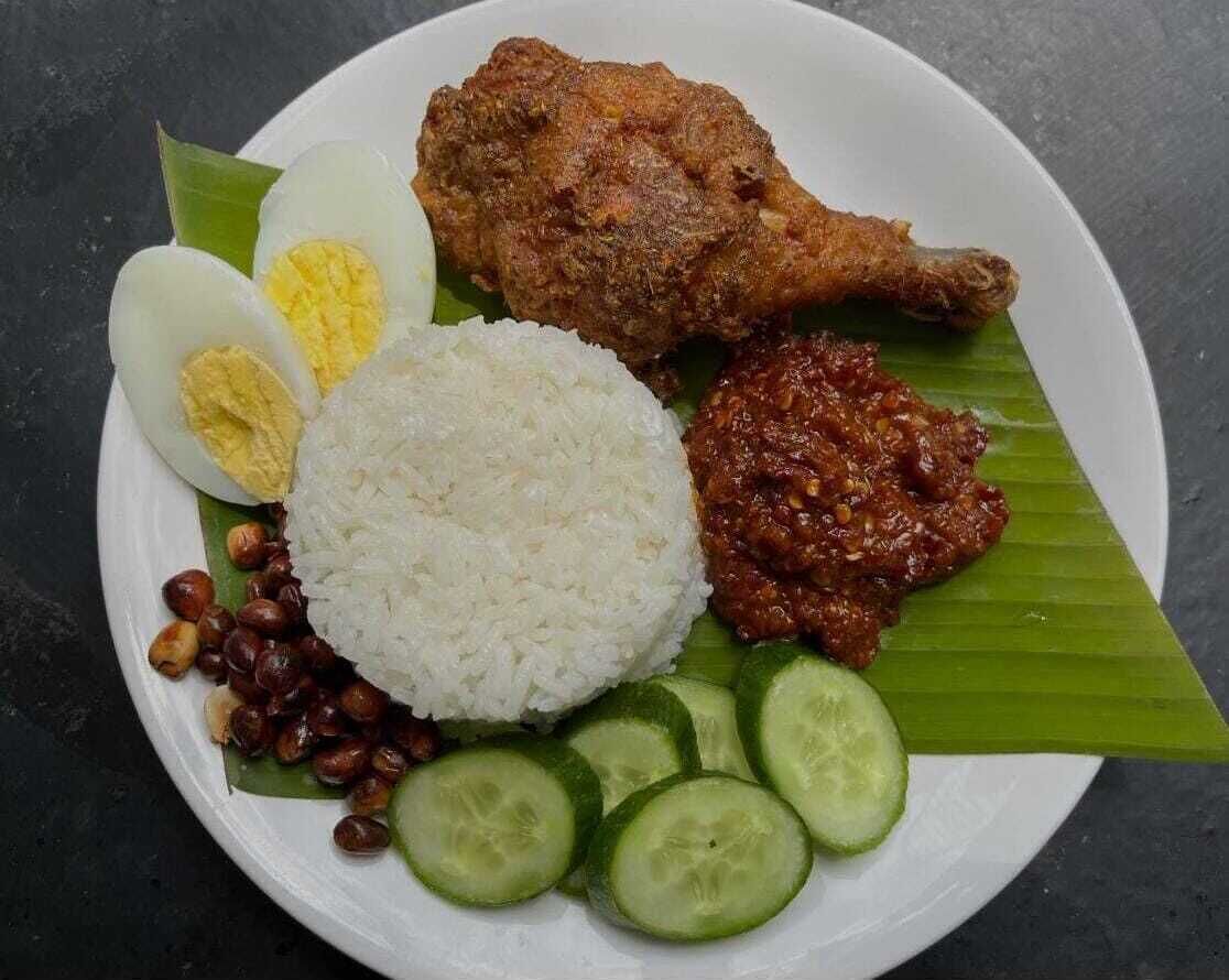 A plate of food with rice, boiled egg, fried chicken, sambal, peanuts, and cucumber slices.