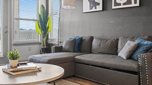 Een moderne woonkamer met een grijze hoekbank, een ronde salontafel en een potplant.