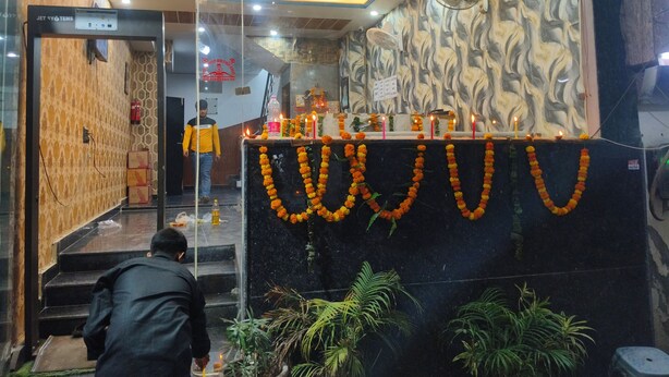 A hotel lobby with a modern ceiling design, a reception desk adorned with marigold garlands, and a staircase leading to the upper floors. - The Grace b&B (New Delhi)