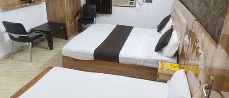 A hotel room with two single beds, a desk, a chair, a TV mounted on the wall, and an air conditioning unit.
