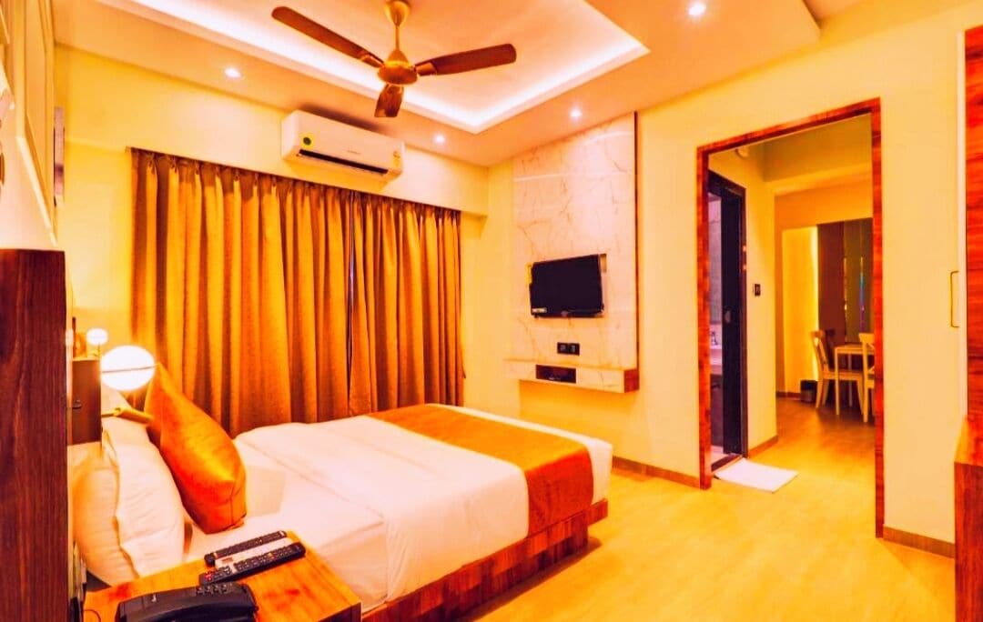 A hotel room with a bed, ceiling fan, TV, and a view of the dining area.